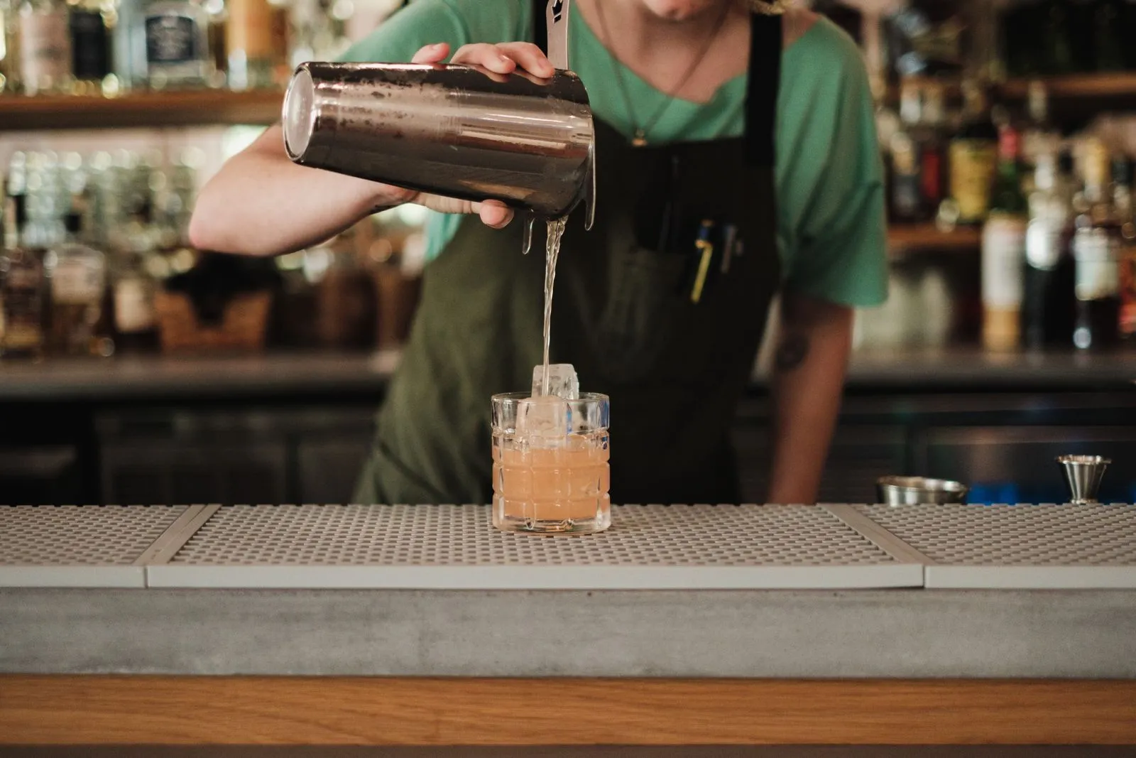 A bartender pours a cocktail into a glass at a stylish bar, showcasing expert preparation.